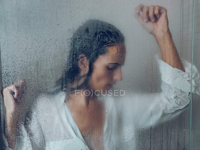 Sopping mujer en camisa posando en cabina de ducha - foto de stock