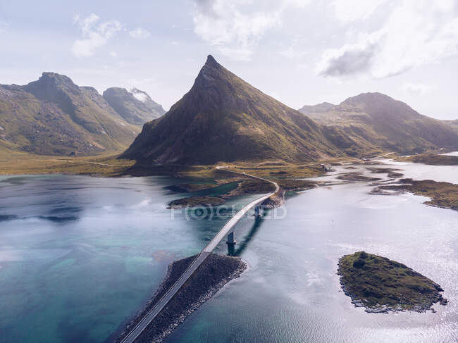 Pintoresca vista del dron de las montañas y la carretera con puente que corre entre el agua azul del océano de las Islas Lofoten - foto de stock
