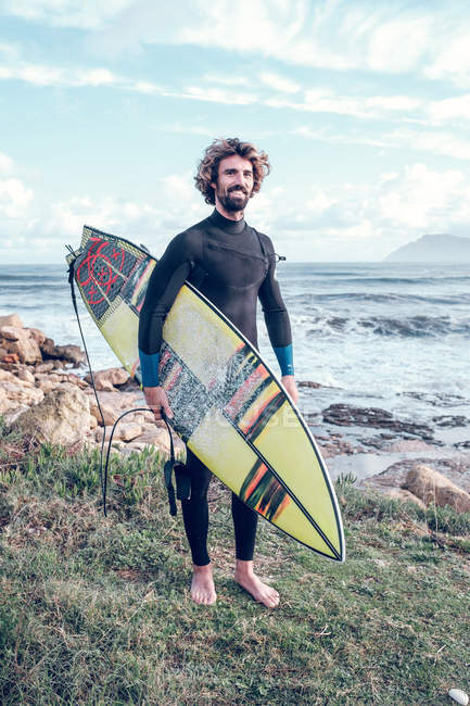 Retrato de um jovem de fato de mergulho com prancha de surf perto do mar — Fotografia de Stock