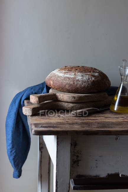 Fresh wholegrain bread loaf on rustic wooden table with bottle of oil — Stock Photo