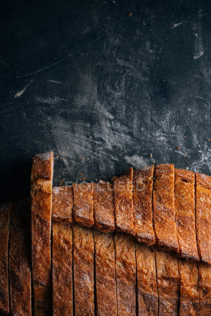Slices of homemade rustic bread on dark background — Stock Photo