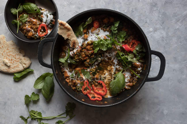 Olla de ragú con lentejas y batata al curry y un tazón en la mesa gris - foto de stock