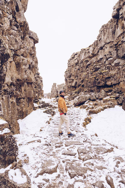 Вид сзади Молодой парень собирается в ущелье со снегом между каменными холмами в Исландии — стоковое фото