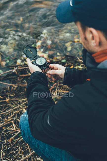 Jovem segurando uma bússola na montanha ao lado de um rio com fundo de cor marrom — Fotografia de Stock