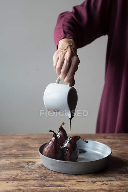 Unrecognizable woman pouring wine syrup of delicious pears while standing near wooden table — Stock Photo