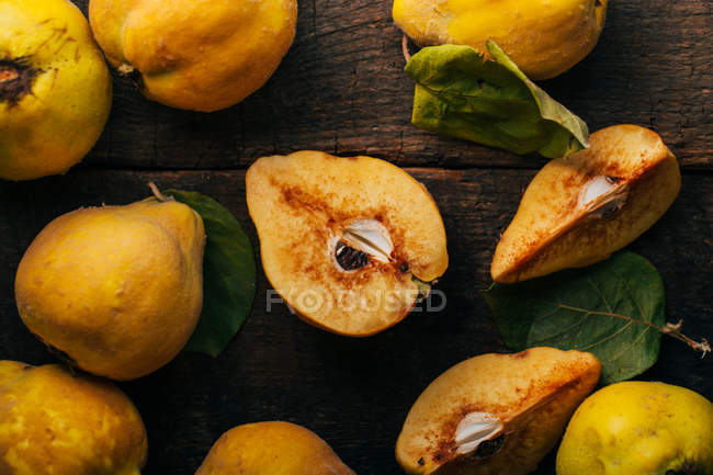Fresh whole and halved quinces on dark wooden background — Stock Photo
