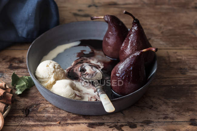 Petite cuillère dans un bol en métal avec de la crème glacée fondante et de savoureuses poires cuites au vin — Photo de stock