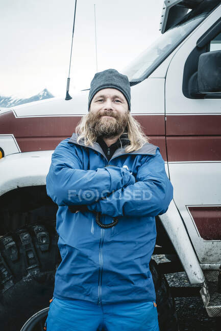 Confident adult bearded man in outwear leaning on off road car with arms crossed looking at camera, Iceland — Stock Photo