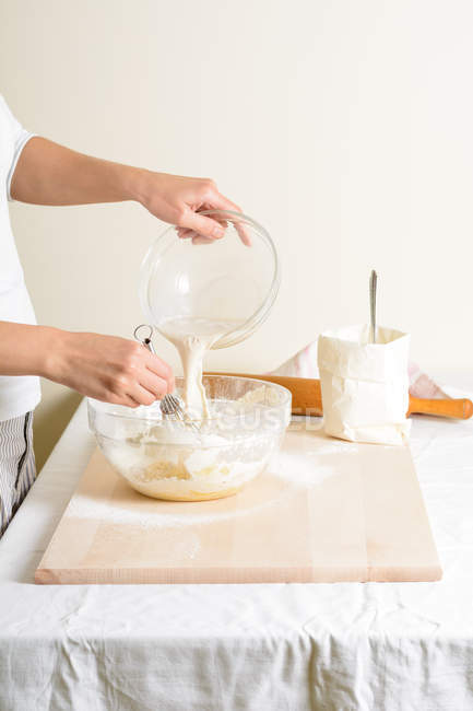 Cortado de mulher derramando leite em tigela na cozinha . — Fotografia de Stock