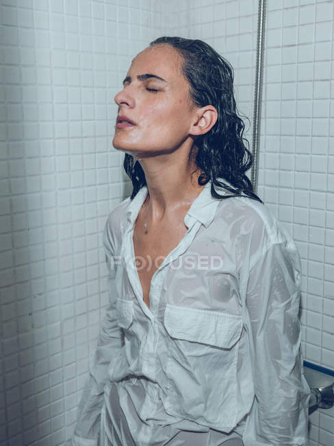 Esguichando mulher em camisa de pé no chuveiro — Fotografia de Stock