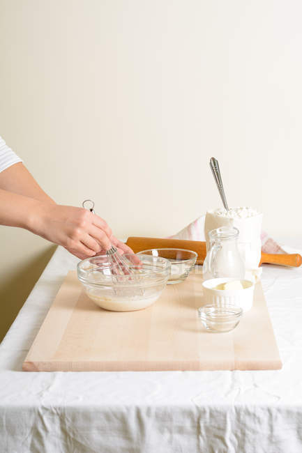 Обрізаний руками жінки, що б'є молоко в мисці на кухні . — стокове фото