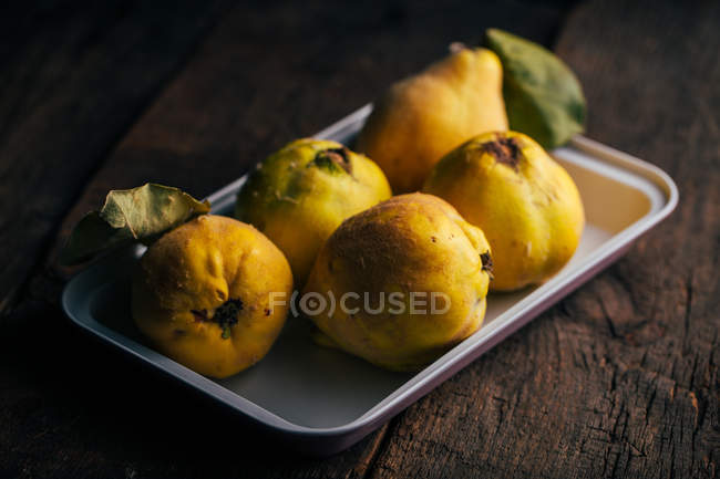 Fresh ripe quinces on tray on dark wooden background — Stock Photo