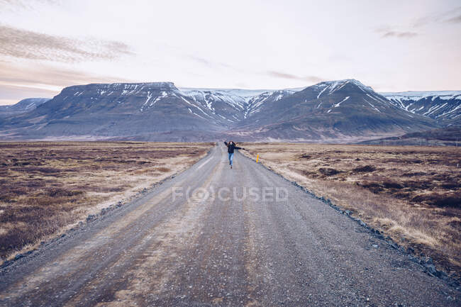 Mensch läuft mit Händen zur Seite auf Landstraße zwischen wildem Land auf Gebirgshintergrund in Island — Stockfoto