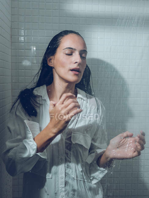 Женщина одета влажно стоя в душе под брызгающей водой — стоковое фото