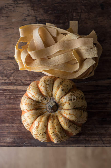 Heap of uncooked pappardelle spaghetti and fresh pumpkin on wooden table — Stock Photo