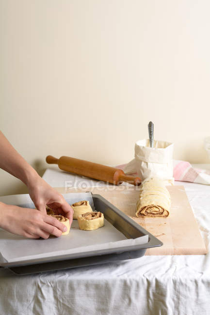 Manos de mujer anónima poniendo pequeños bollos crudos en la bandeja para hornear en la cocina ligera . - foto de stock