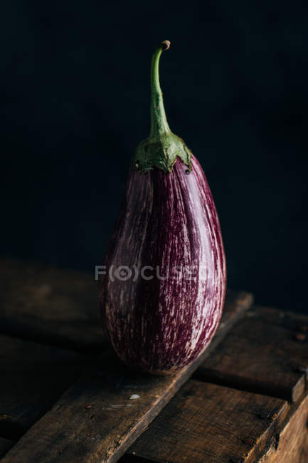 Fresh striped eggplant on wooden table on dark background — Stock Photo