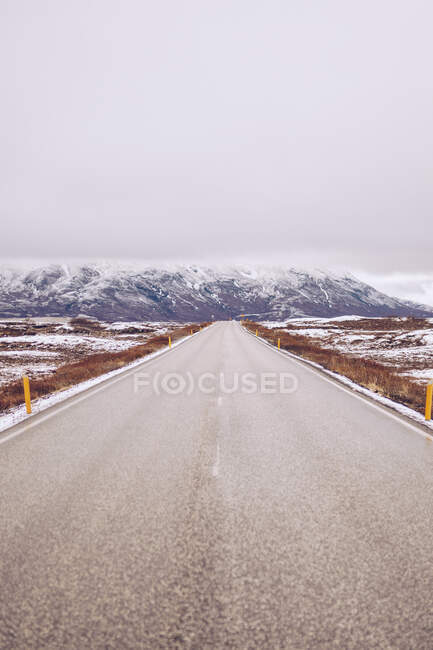 Countryside road between wild lands in snow leading to mountains and sky in clouds in Iceland — Stock Photo