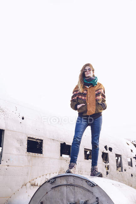 Junge Frau in warmer Kleidung in kaputtem Flugzeug zwischen düsterem Gelände in Island — Stockfoto