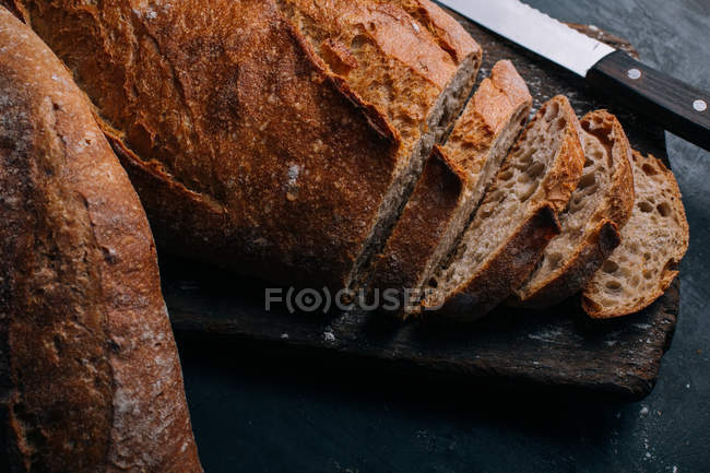 Частично нарезанный домашний деревенский хлеб на деревянной доске — стоковое фото