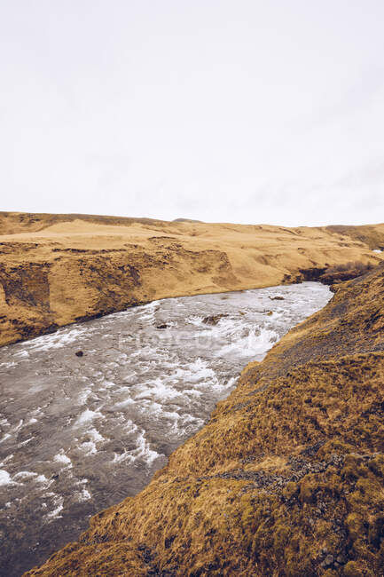 Mountain river with water cascade between brown stone hills and view on?lowland in Iceland — Stock Photo