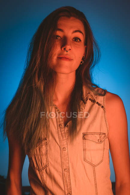 Charming young lady with piercing looking at camera in redness on blue background — Stock Photo