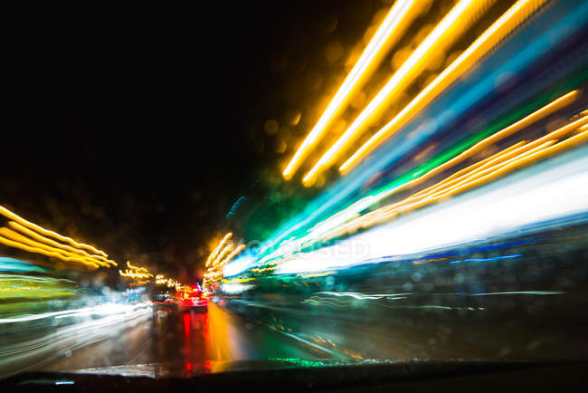 Abstract view of bright trail lights through automobile window at night — Stock Photo