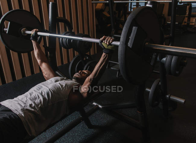 Черный мужчина поднимает тяжелую штангу в спортзале — стоковое фото