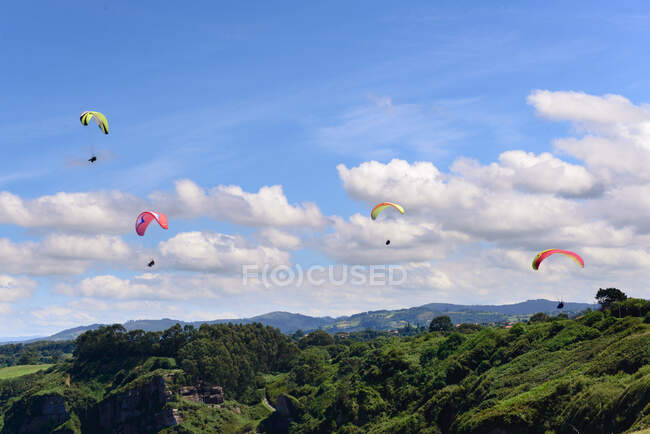 Magnificent drone view of bright paragliders flying against cloudy sky over beautiful green nature on sunny day — Stock Photo
