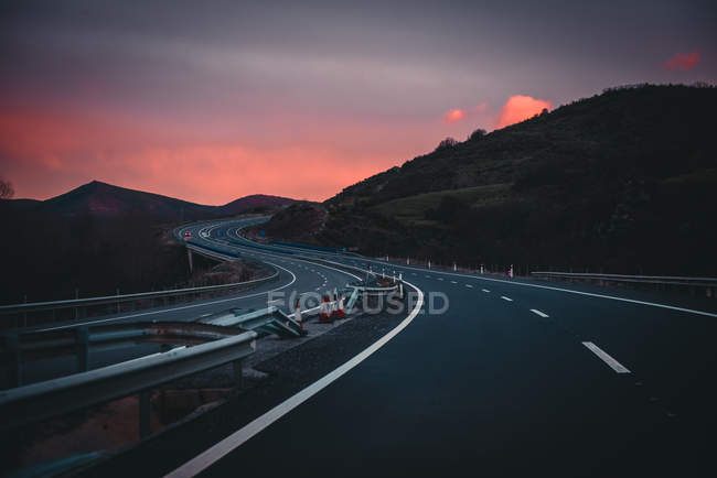 Estrada nas montanhas ao pôr-do-sol com céu dramático — Fotografia de Stock