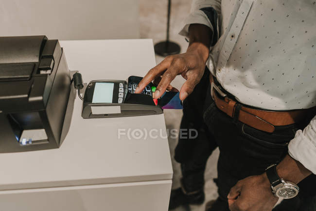 Сверху снимок руки афроамериканца, нажимающего кнопки на клавиатуре современного платежного терминала — стоковое фото