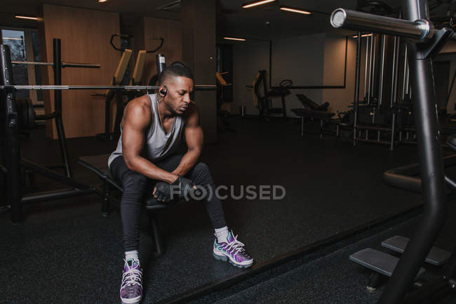 Hombre negro en auriculares sentado en la máquina de ejercicio - foto de stock