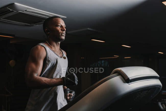 Seitenansicht eines gut aussehenden afrikanisch-amerikanischen Typen in Sportbekleidung, der Musik hört und auf dem Laufband läuft — Stockfoto