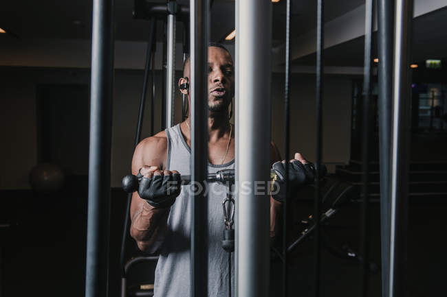 Handsome African American guy in earphones exercising on machine while working out in modern gym — Stock Photo
