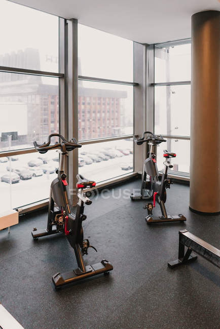 Duas bicicletas de exercício modernas em pé perto de uma enorme janela dentro de um ginásio elegante — Fotografia de Stock