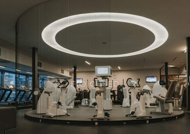 Verschiedene moderne Trainingsgeräte stehen im Kreis unter riesigen Lampen im stilvollen Fitnessraum — Stockfoto