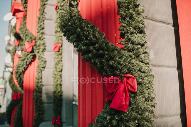 Fluffy conifer garlands with bows hanging on red pillars near walls of lovely building on sunny day — Stock Photo