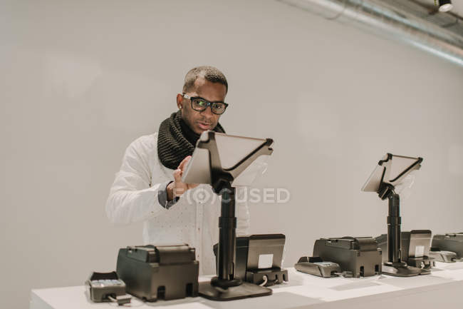 Vista lateral del hombre afroamericano guapo en traje de moda de pie cerca del mostrador en la tienda elegante y el uso de caja registradora - foto de stock