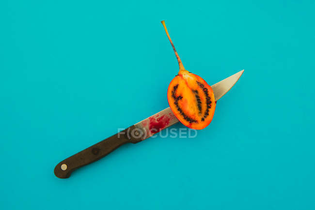Гострий ніж, що нарізає смачно стиглий тамарілло на яскраво-синьому фоні — стокове фото