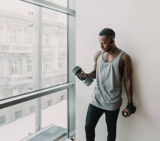Черный мужчина с гантелями в спортзале — стоковое фото