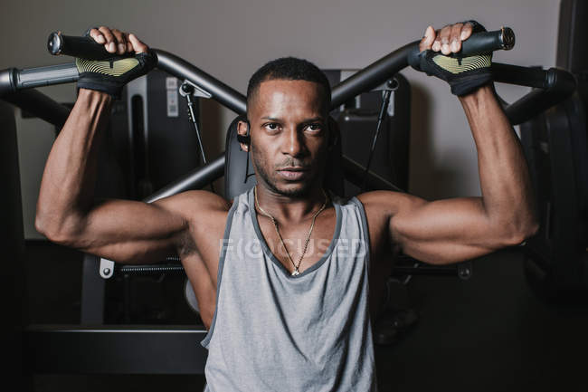 Serious African American guy listening to music and performing exercise on modern machine during workout in gym — Stock Photo