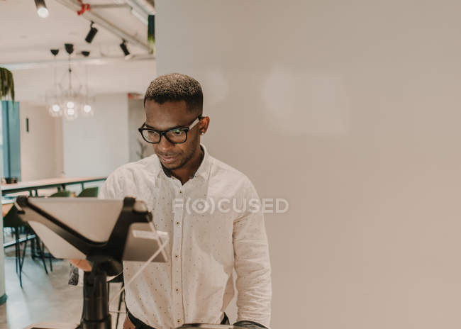 Нахабний афроамериканець у модному одязі стоїть біля прилавка в стильній крамниці і користується касовим апаратом. — стокове фото