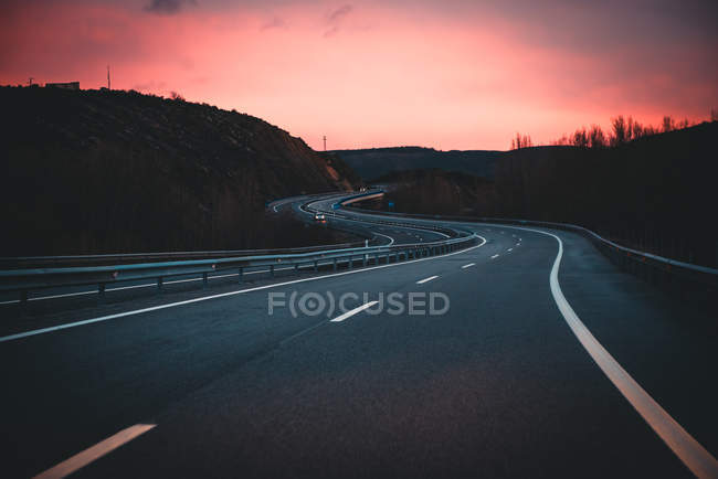 Autostrada in montagna al tramonto con cielo drammatico — Foto stock