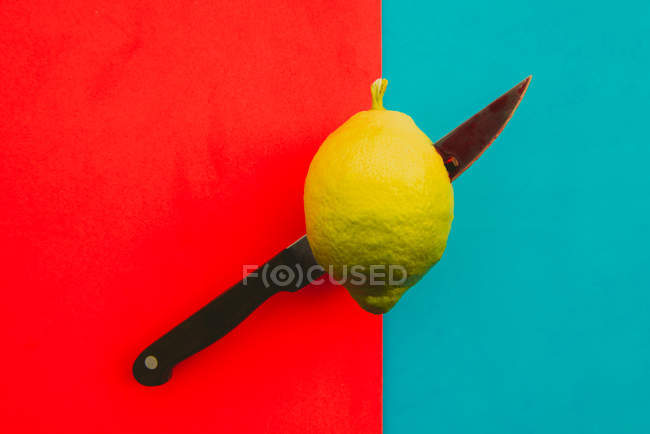 Scharfes Messer schneidet saftige reife Zitrone auf lebendigem roten und blauen Hintergrund — Stockfoto