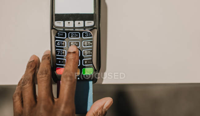 De arriba tiro de mano del hombre afroamericano pulsando botones en el teclado de la terminal de pago moderna - foto de stock