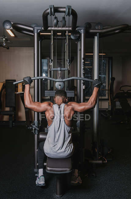 Hombre negro haciendo ejercicio en la máquina en el gimnasio - foto de stock