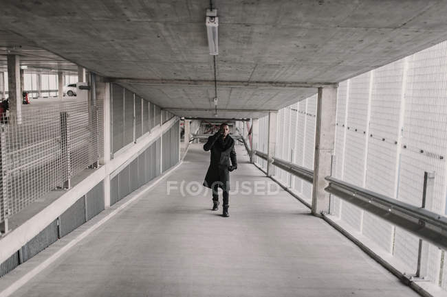 African American man in stylish outfit walking in passage of modern building and having smartphone conversation — Stock Photo