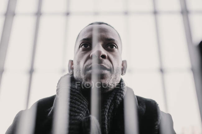 From below shot of handsome African American man in stylish clothes standing behind fence on city street — Stock Photo