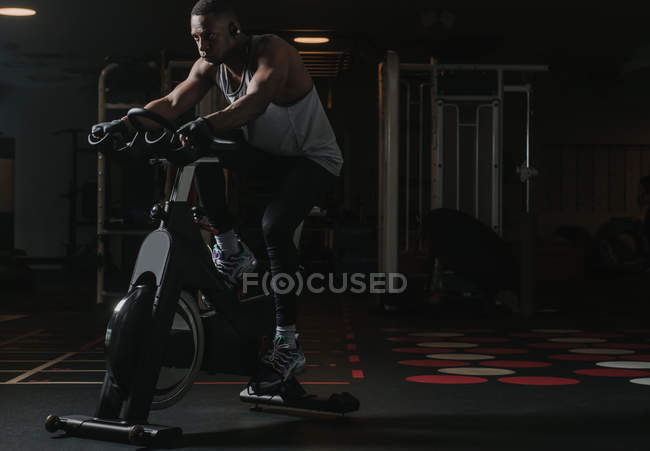 Homem negro sério em bicicleta de exercício no ginásio — Fotografia de Stock