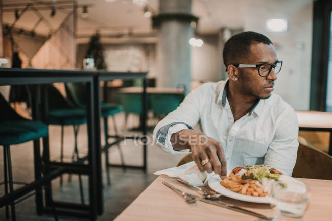 Uomo afroamericano adulto che si gode il cibo delizioso mentre è seduto a tavola in un ristorante elegante — Foto stock